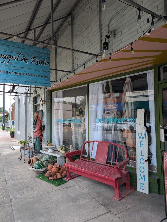A storefront with a red bench and welcome sign. Sign reads