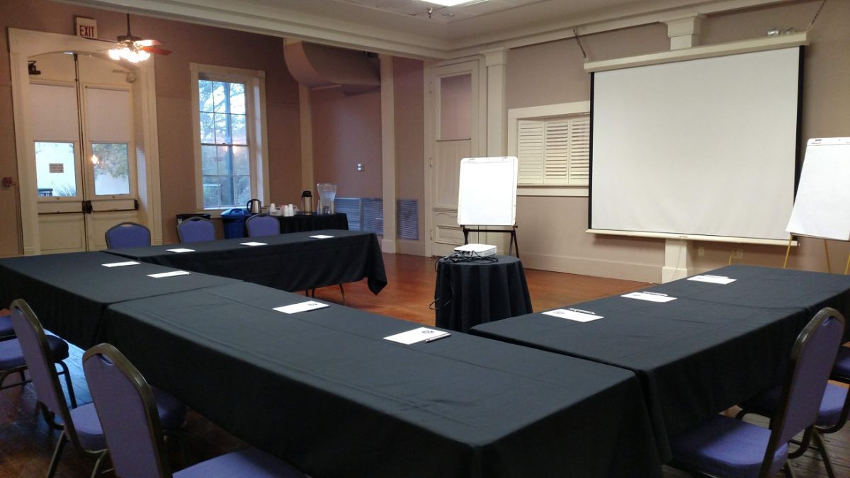 A conference room with tables and chairs and a projector screen