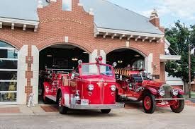Two vintage red fire trucks parked inside and in front of a historic brick fire station.