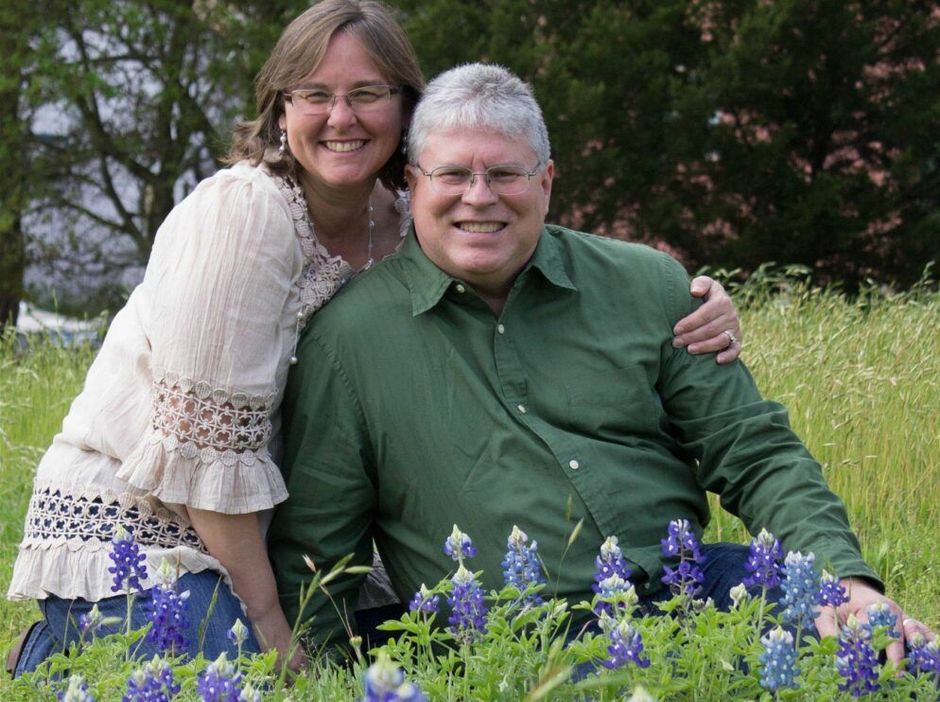 A man and a woman are posing for a picture in a field of flowers.