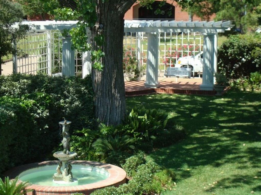 A fountain in a garden with a pergola in the background