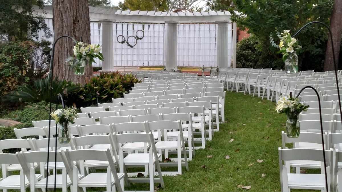 A row of white folding chairs are lined up in the grass for a wedding ceremony.