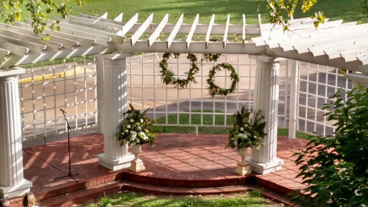 A white pergola with flowers and wreaths on it.