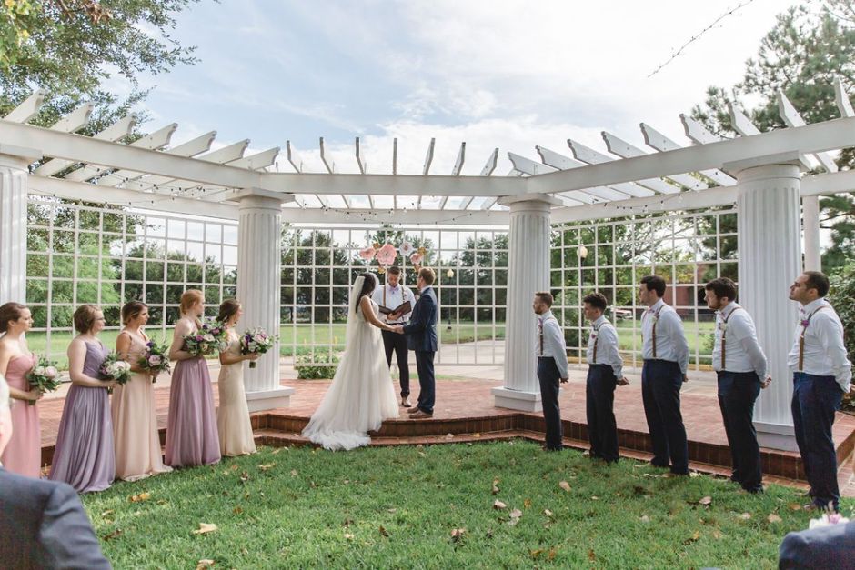 A bride and groom are getting married under a pergola with their wedding party.