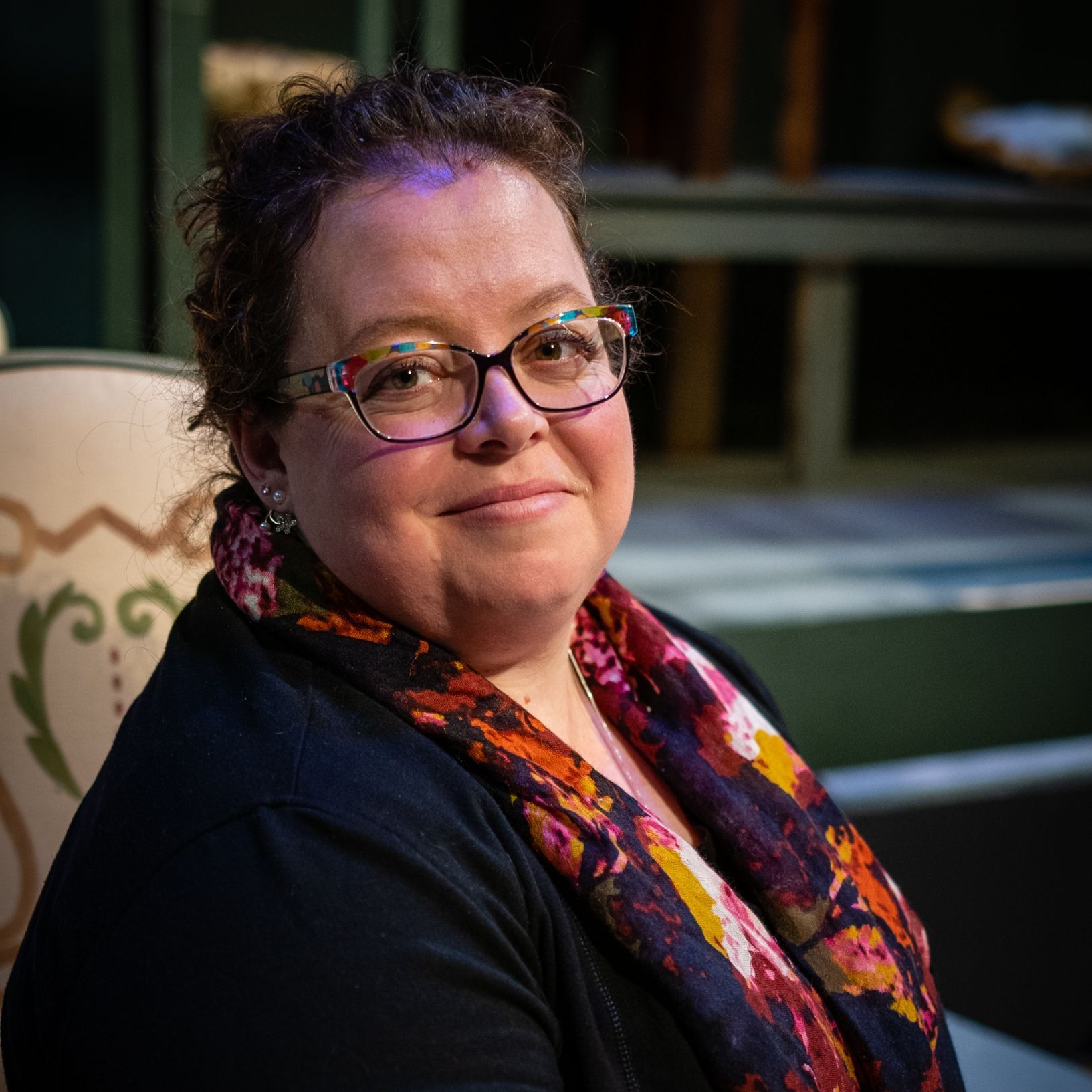 A woman wearing glasses and a scarf is sitting in a chair.