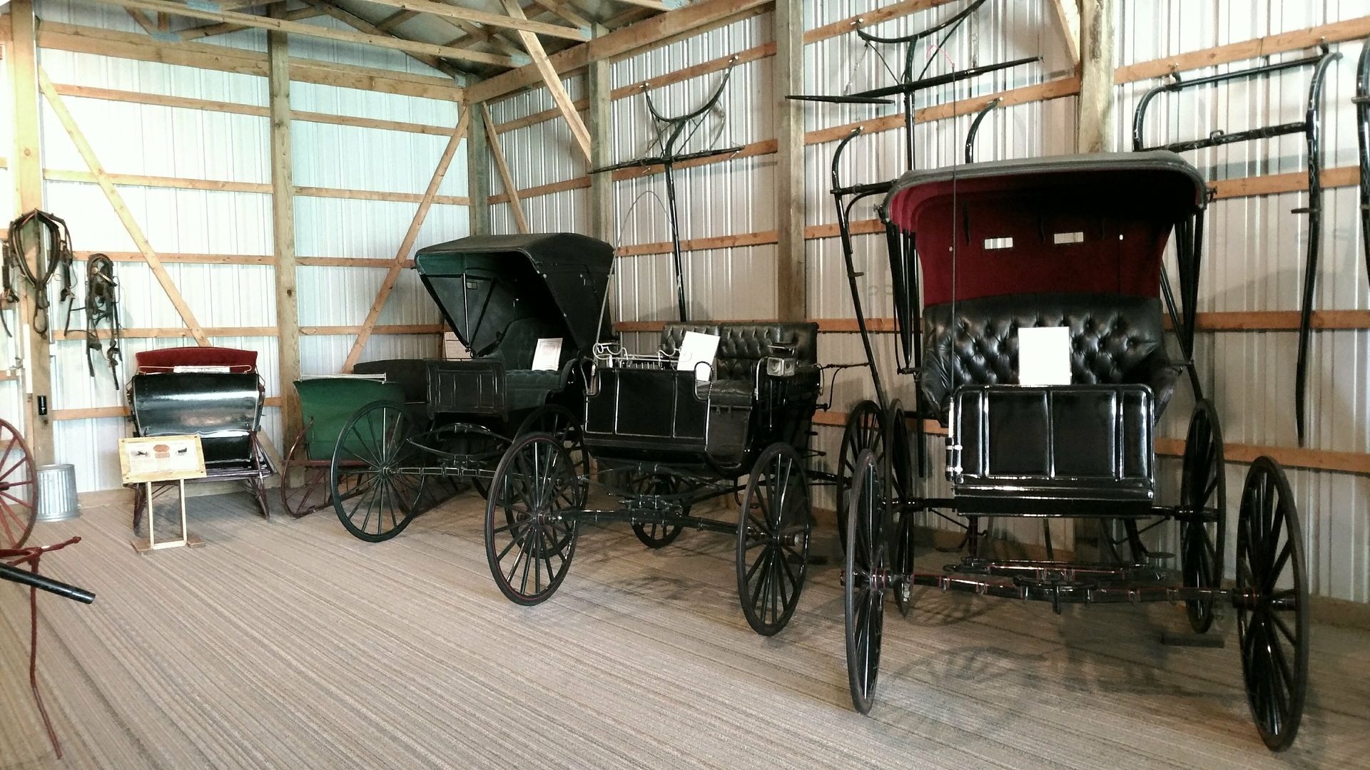 Three horse drawn carriages are lined up in a barn.