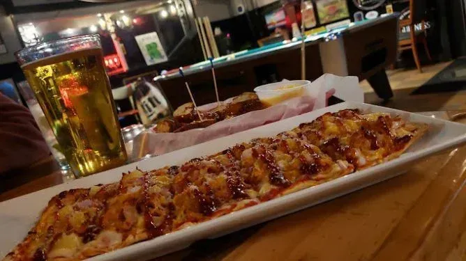 A long pizza on a plate next to a glass of beer on a table.