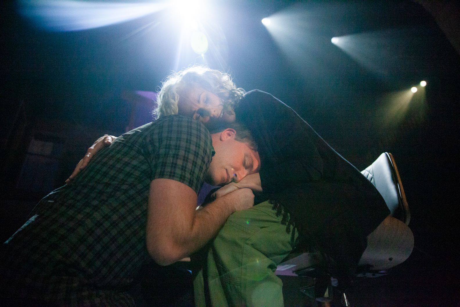 Two people are hugging each other on a stage in a dark room.