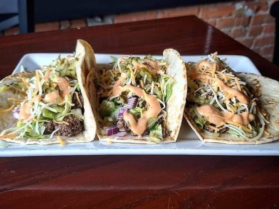 Three tacos are sitting on a white plate on a wooden table.