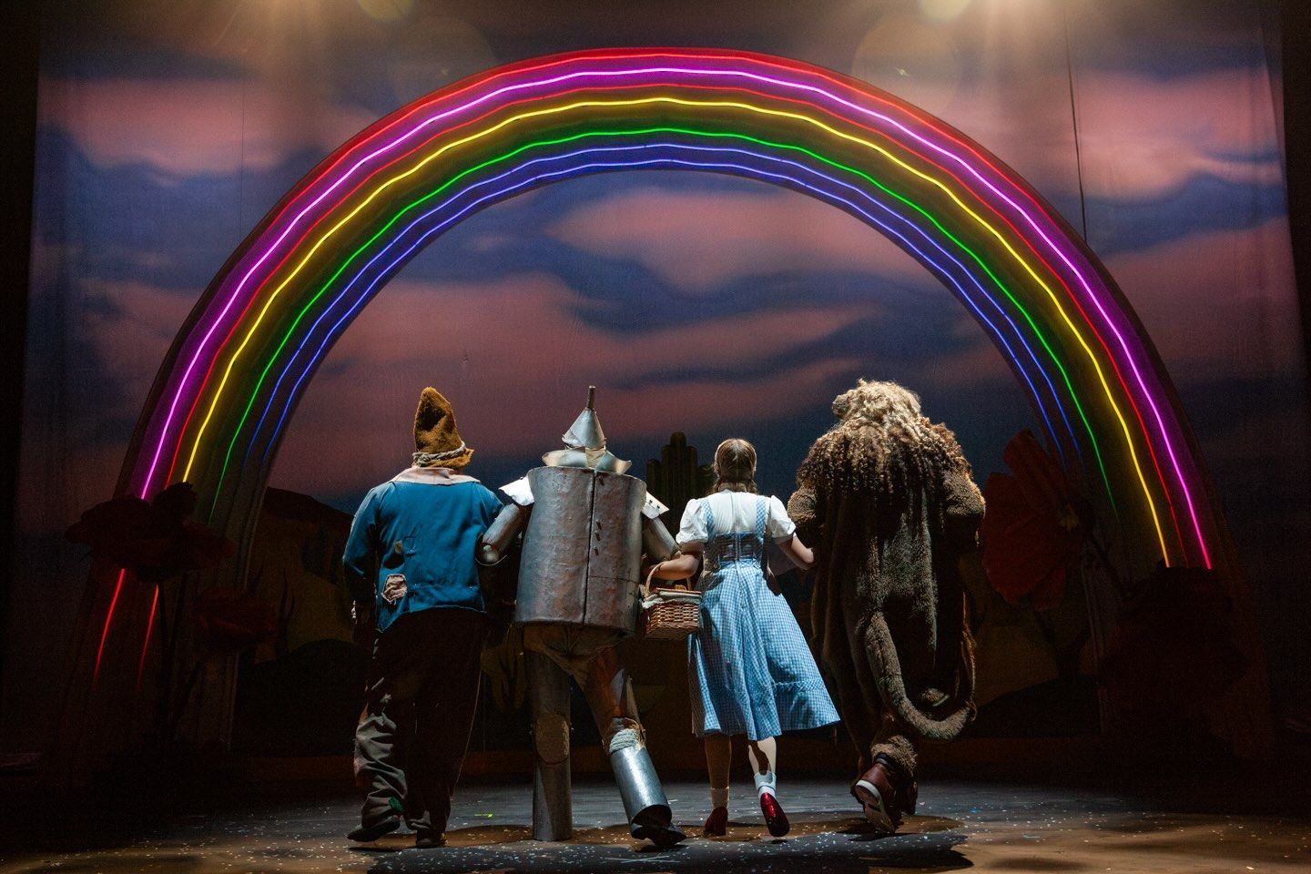 characters from the wizard of oz are skipping under a rainbow.