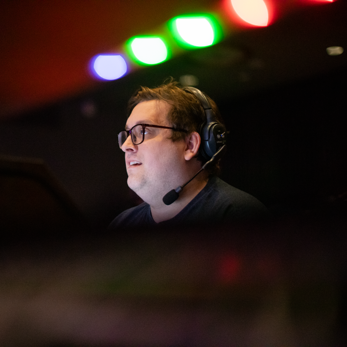 A man wearing headphones and glasses is sitting at a production desk.