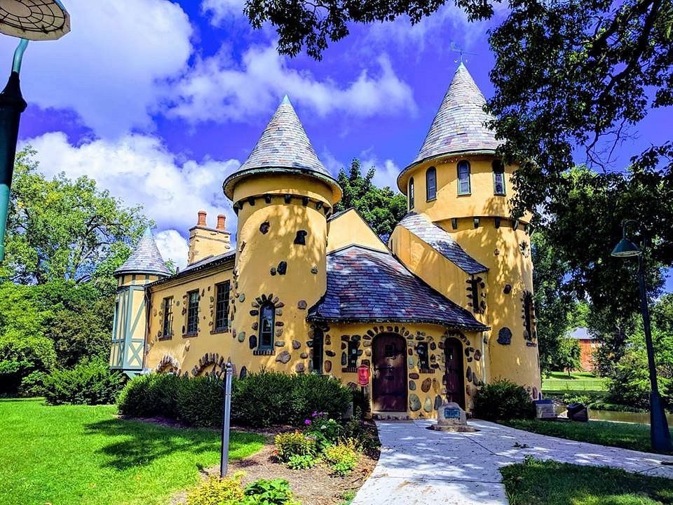 A yellow castle with two towers is surrounded by grass and trees.