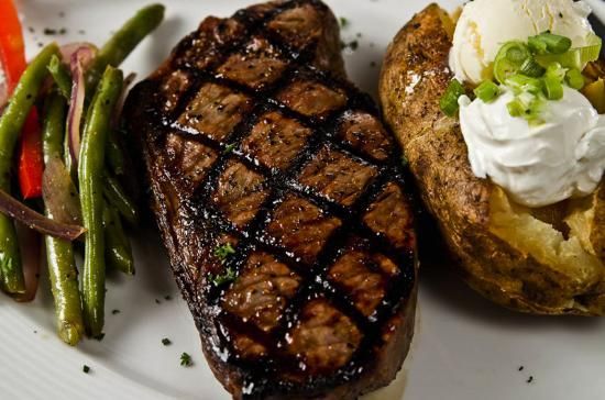 A white plate topped with a steak , potatoes , green beans and sour cream.