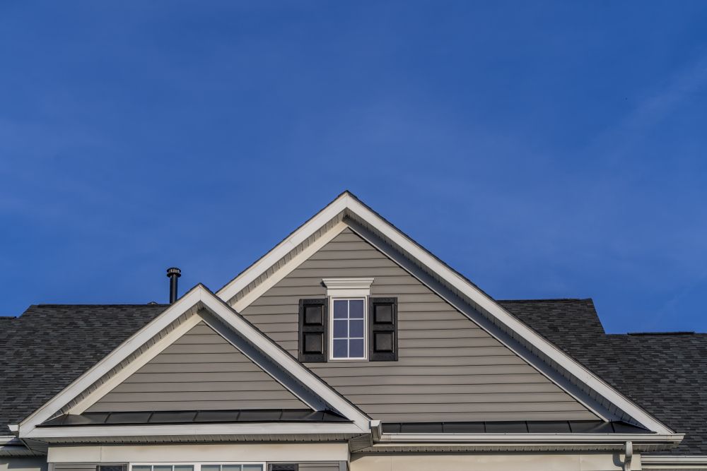 Gabled House Roof With Grey Siding, White Trim, and a Small Black-shuttered Window — GCX Roofing In Brisbane, QLD