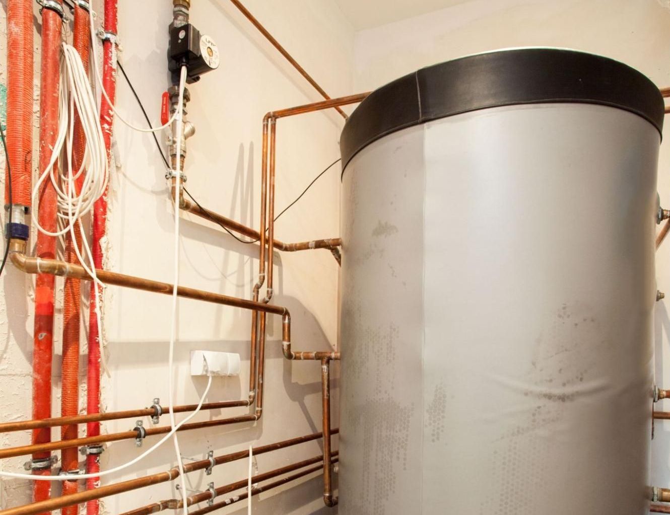 A large stainless steel water heater is sitting in a room with copper pipes.