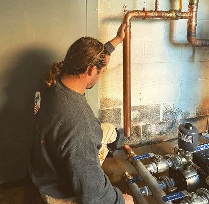 A man is working on a copper pipe in a basement