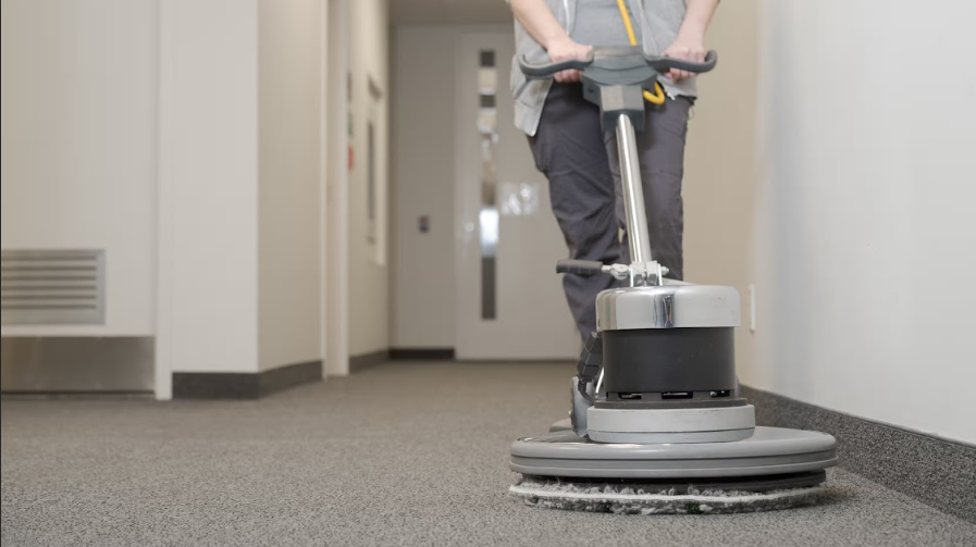 Person steam-cleaning a patterned rug with an industrial cleaner in a living room.