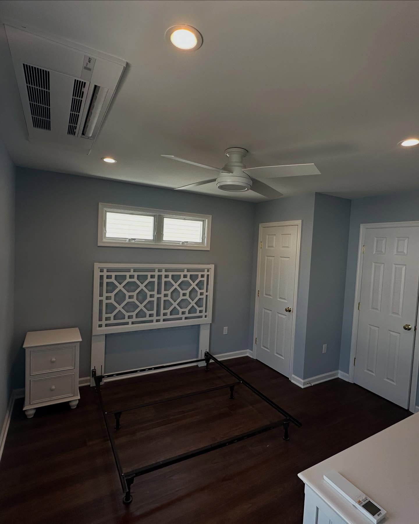 new built bedroom with light blue walls, dark wood floor, white bed frame, headboard, nightstand, and ceiling fan built by j.k. construction llc