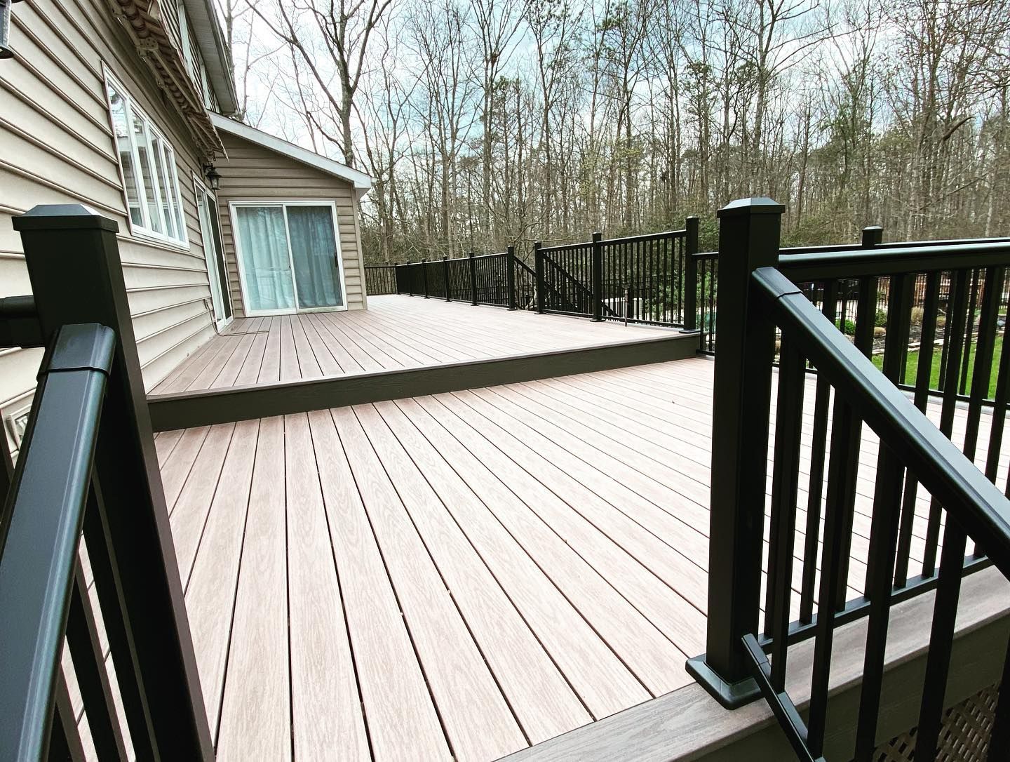 renovation of a wooden deck with dark railing, sliding door, and trees in the background done by j.k. construction llc