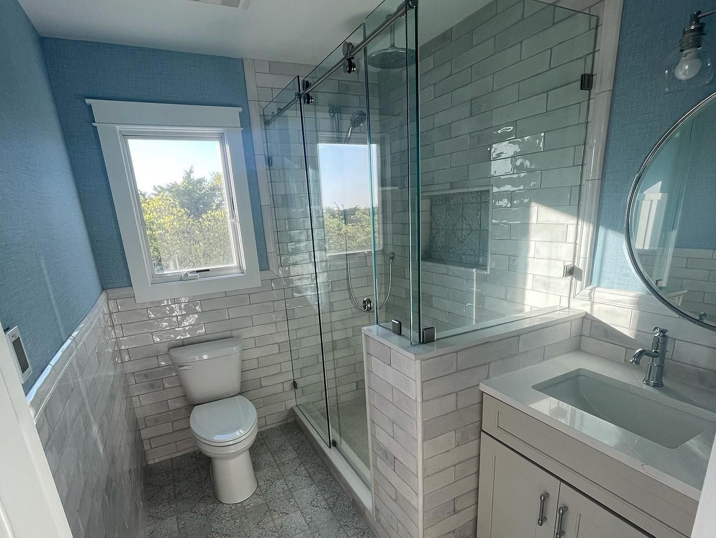 a remodeled modern bathroom with glass shower, white vanity, and blue walls done by j.k. construction llc