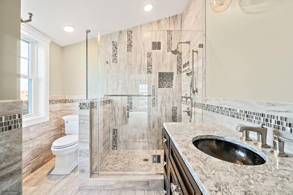 Modern bathroom with glass shower, vanity, toilet, and light-colored marble tile walls and flooring renovated by j.k. construction llc in avalon, new jersey