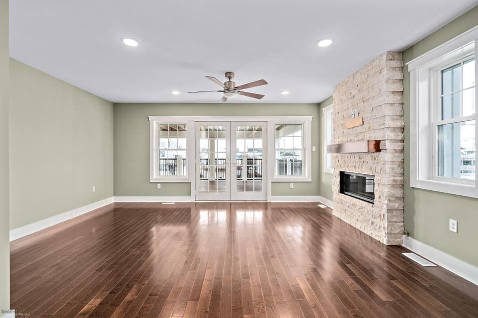 Empty living room with dark wood floors, light green walls, stone fireplace, and French doors remodeled by j.k. construction llc in avalon, new jersey