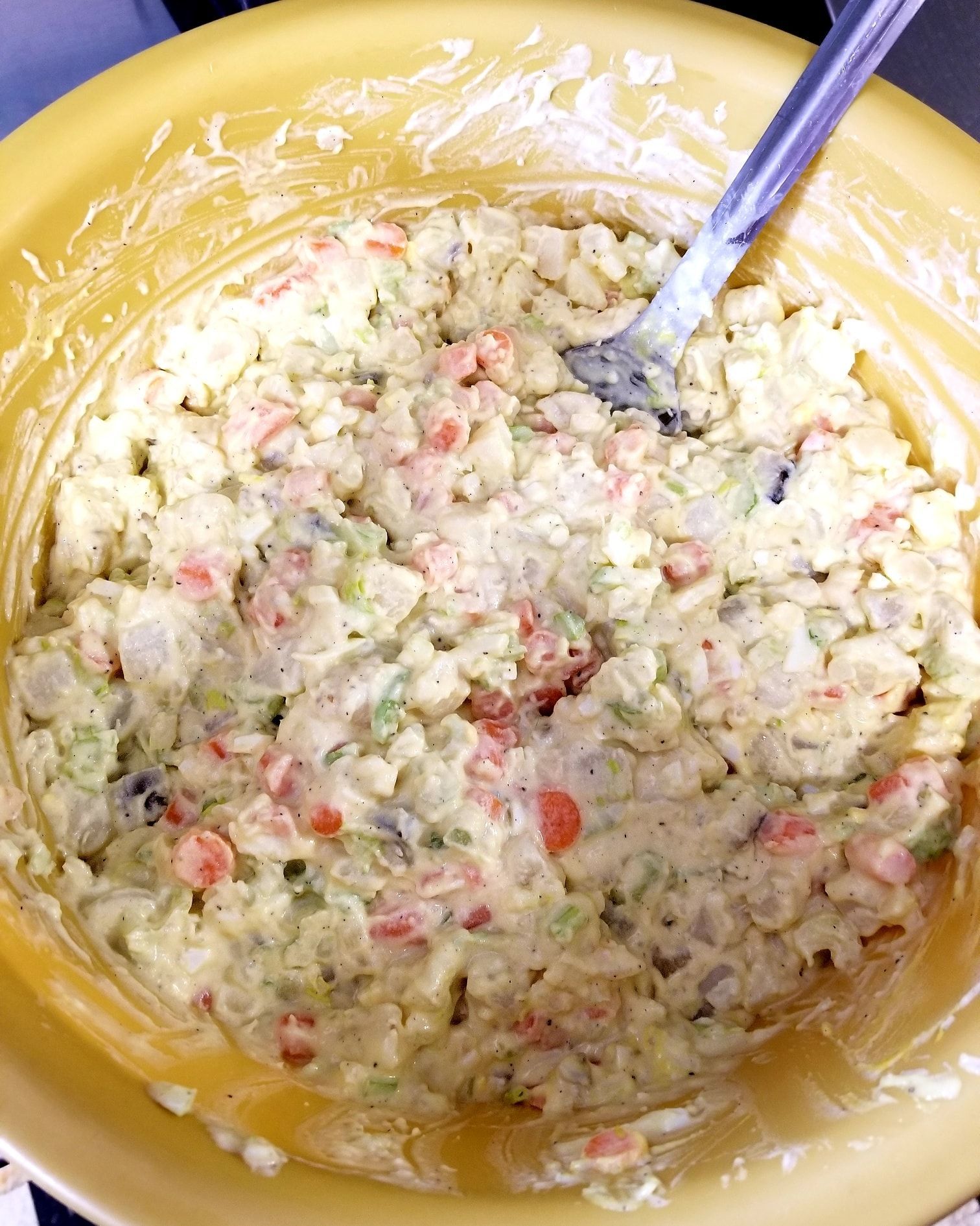 A yellow bowl filled with a salad with a fork in it.