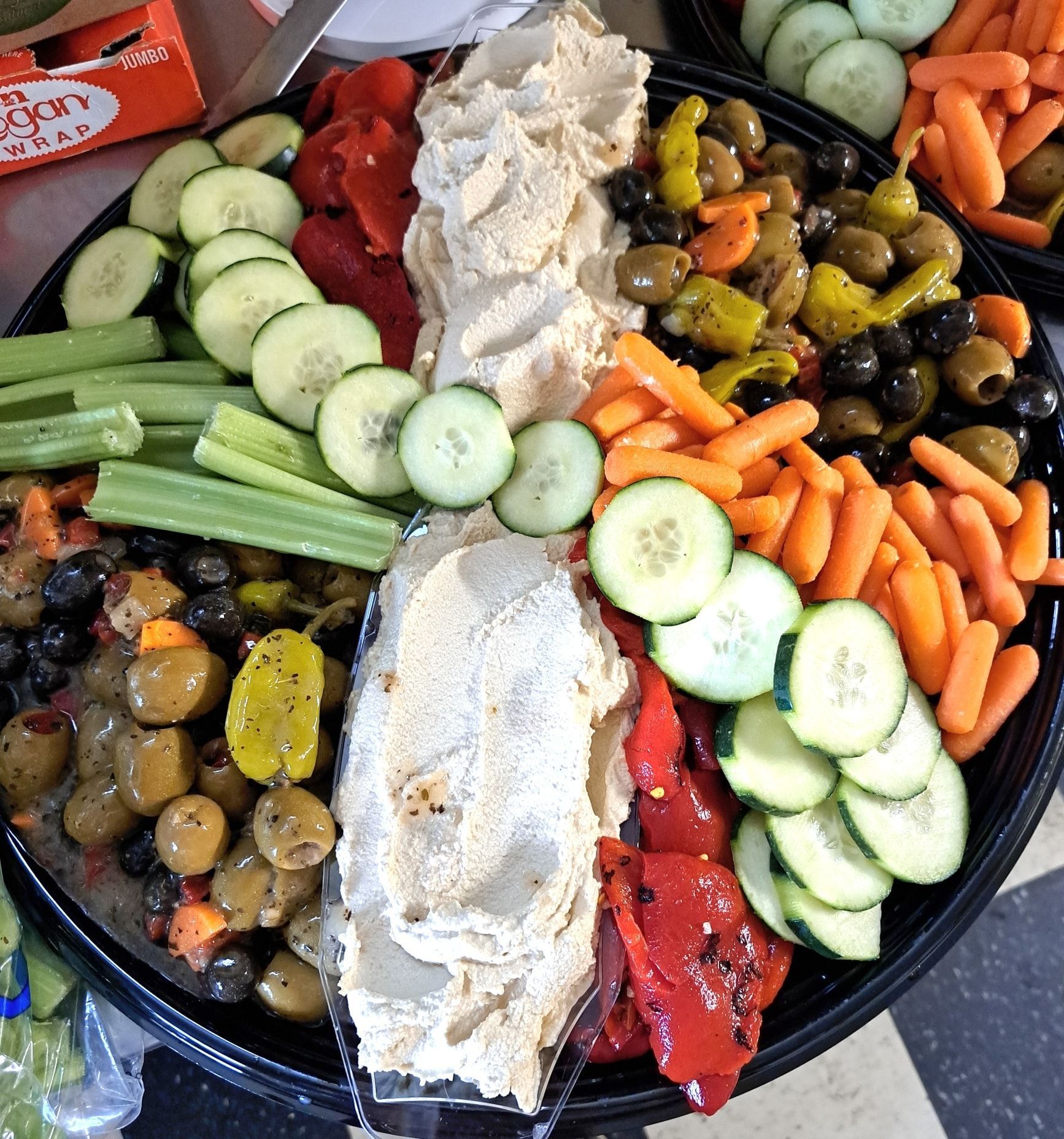 A tray of vegetables including cucumbers carrots olives and hummus