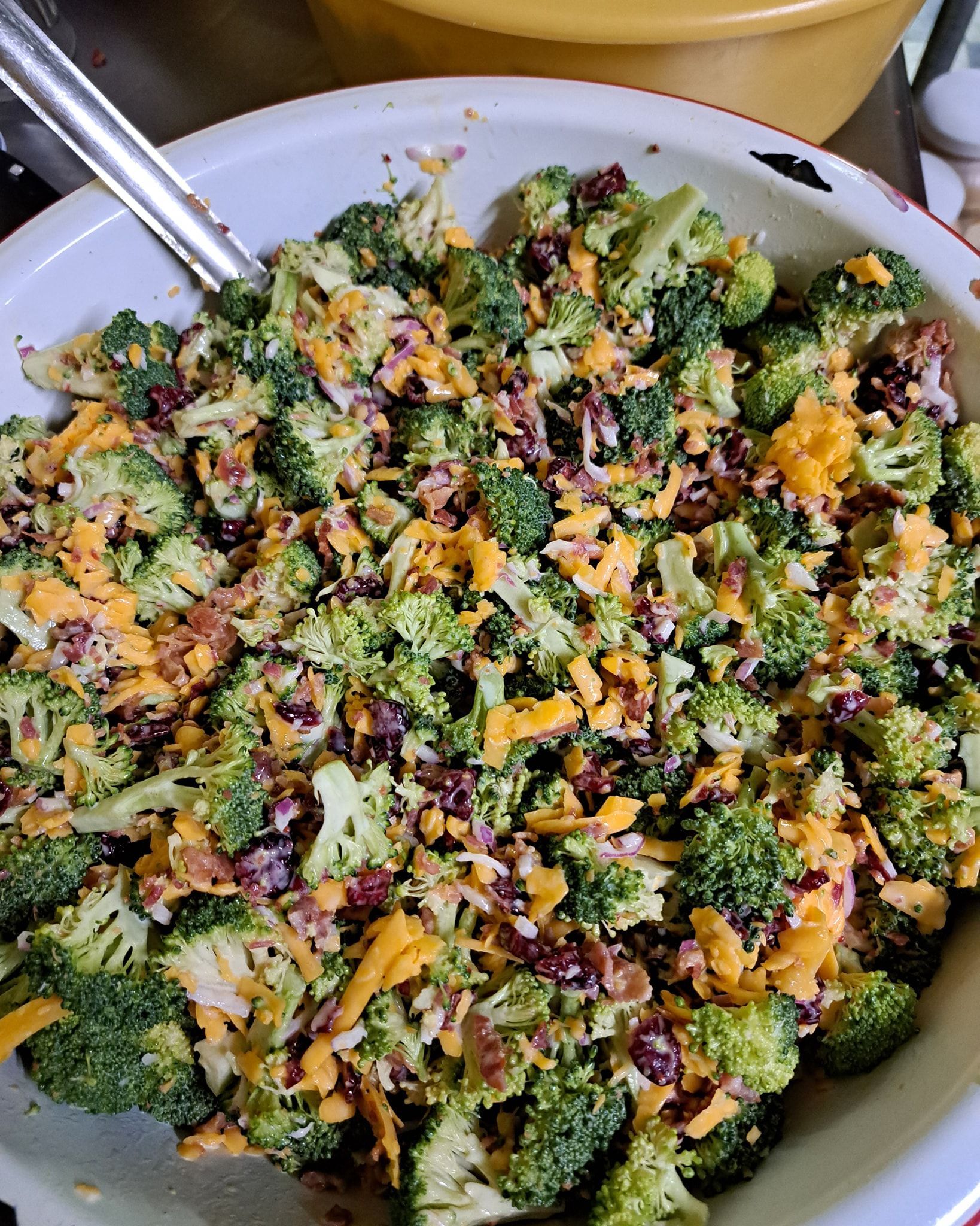 A bowl of broccoli salad with cheese , bacon and cranberries.