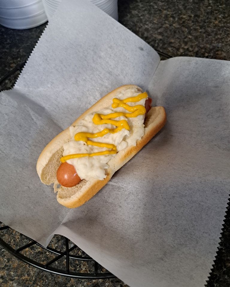 A hot dog with mustard and mashed potatoes on a bun