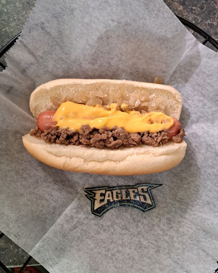 A hot dog on a bun with cheese and eagles logo on it
