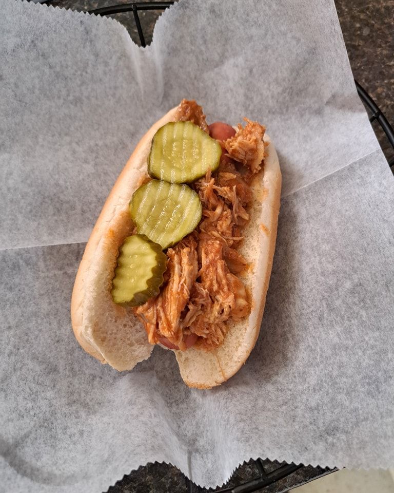 A pulled pork hot dog with pickles on top