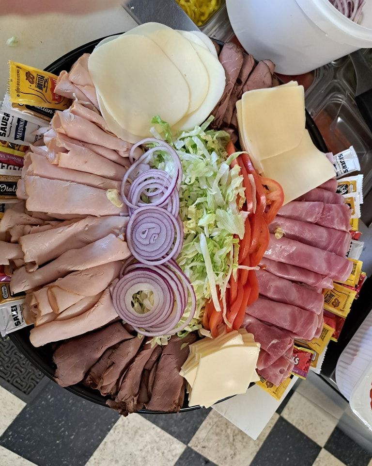 A tray of meats , cheeses , onions , and peppers on a checkered floor.