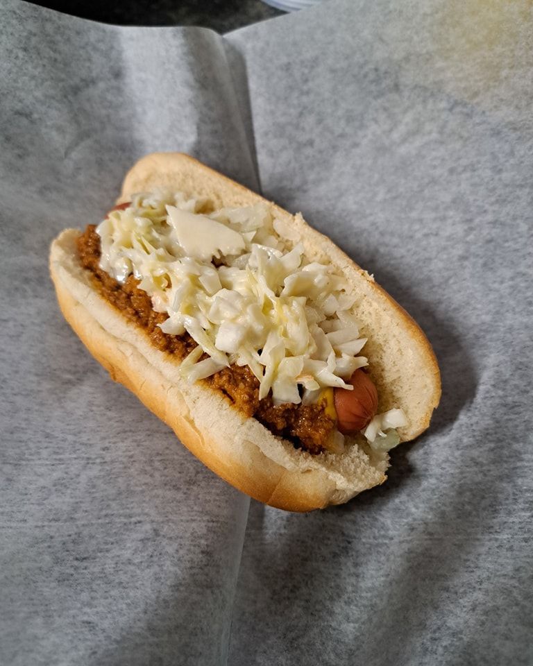 A hot dog with coleslaw and mayonnaise on a bun is sitting on a piece of paper.