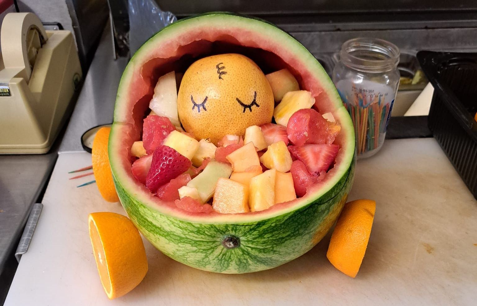 A watermelon filled with fruit is sitting on a cutting board