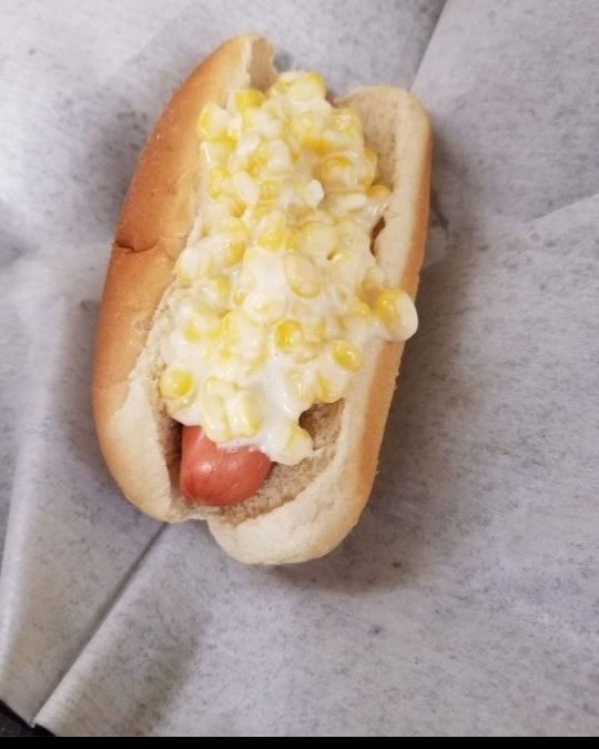 A hot dog with corn and cheese on a bun