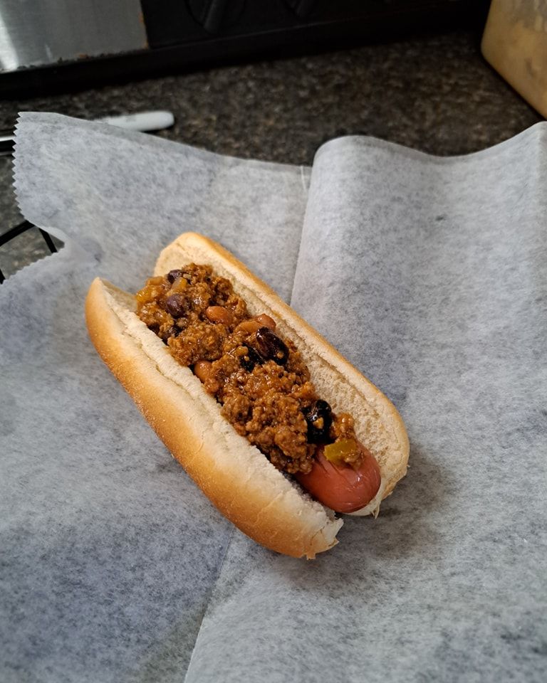 A chili dog is sitting on a piece of wax paper.