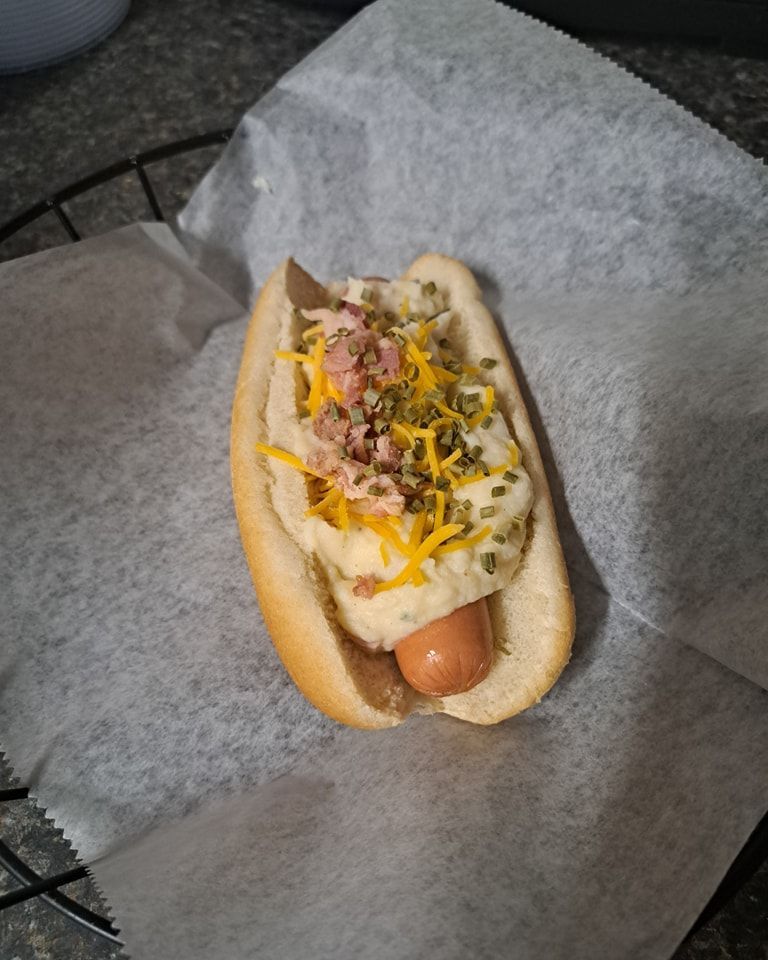 A hot dog with mashed potatoes and cheese on a bun