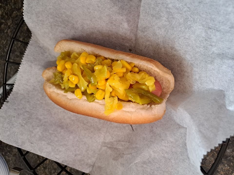 A hot dog with corn and pickles on a bun
