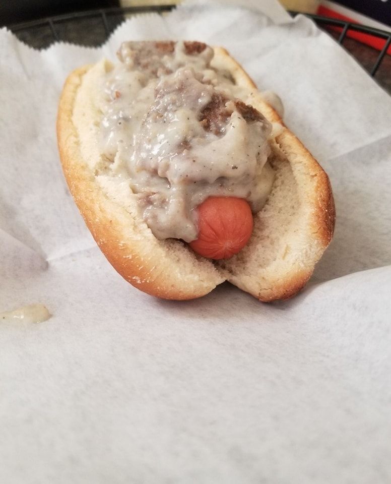 A hot dog with gravy on it is sitting on a piece of paper.