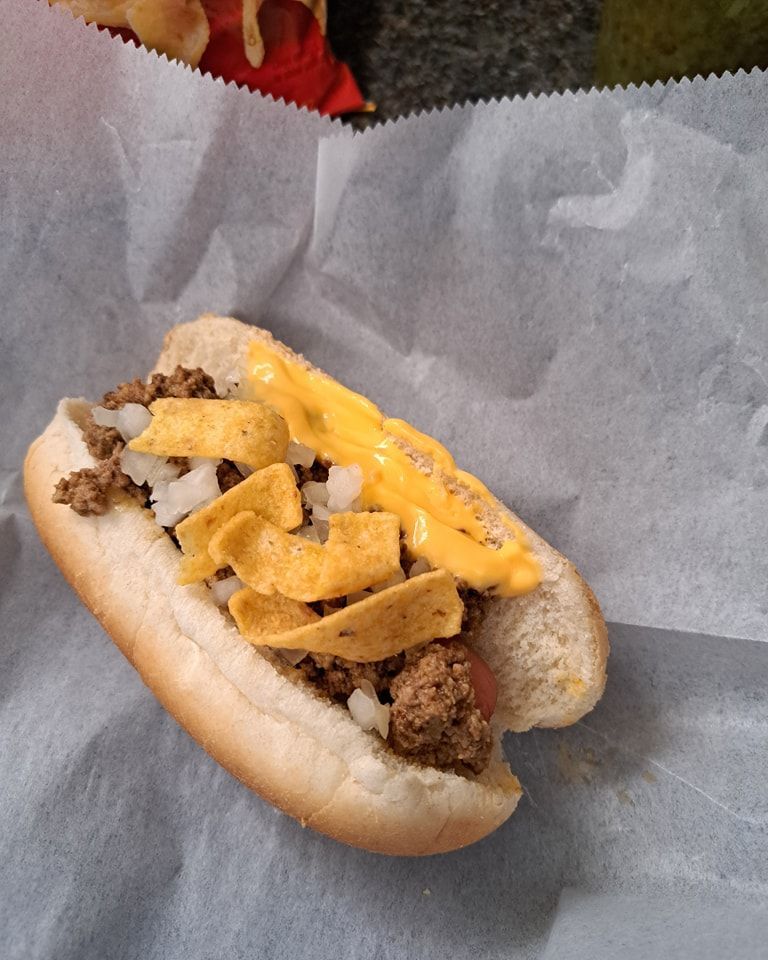 A hot dog with cheese onions and nachos on a bun