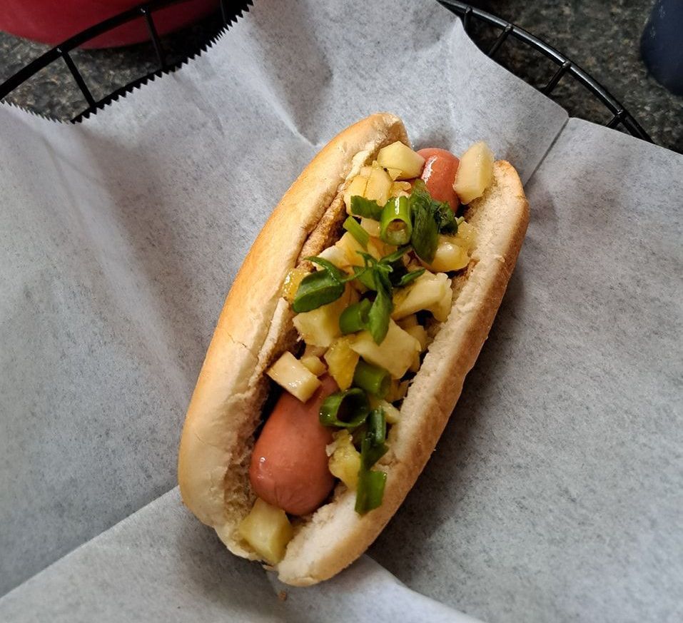 A hot dog with pineapple and green onions on a bun