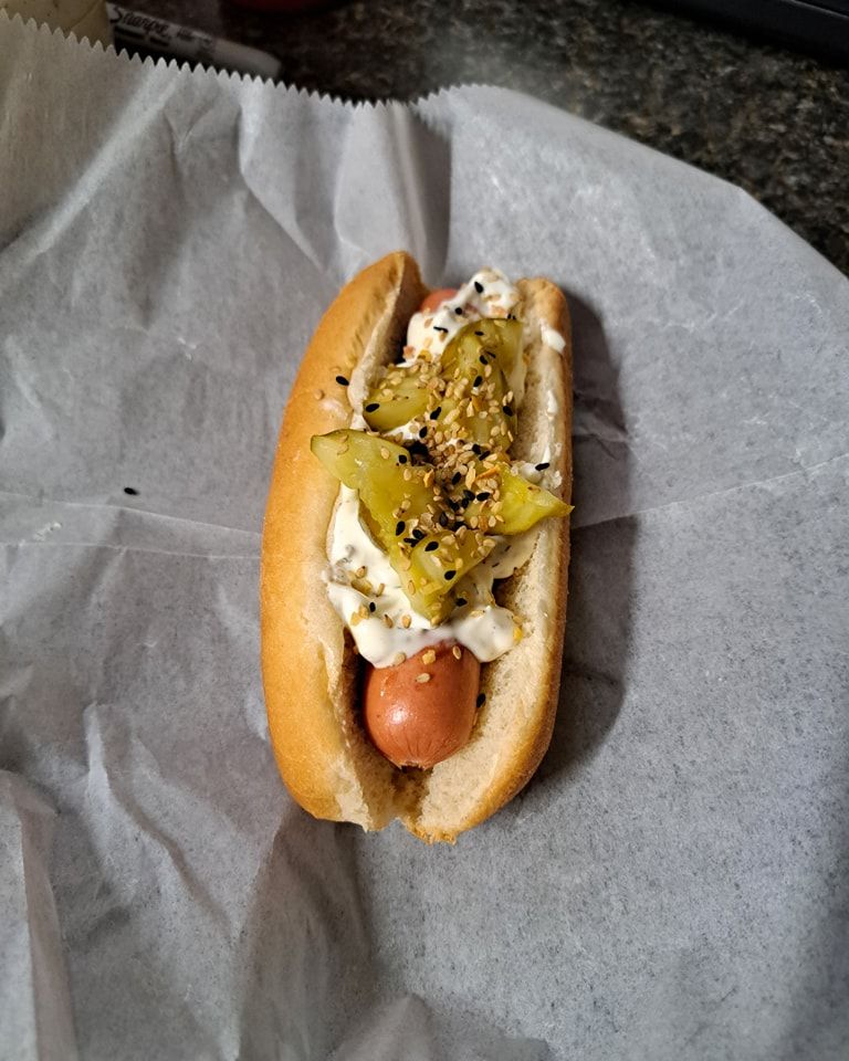 A hot dog with pickles and mustard on a bun is sitting on a piece of wax paper.