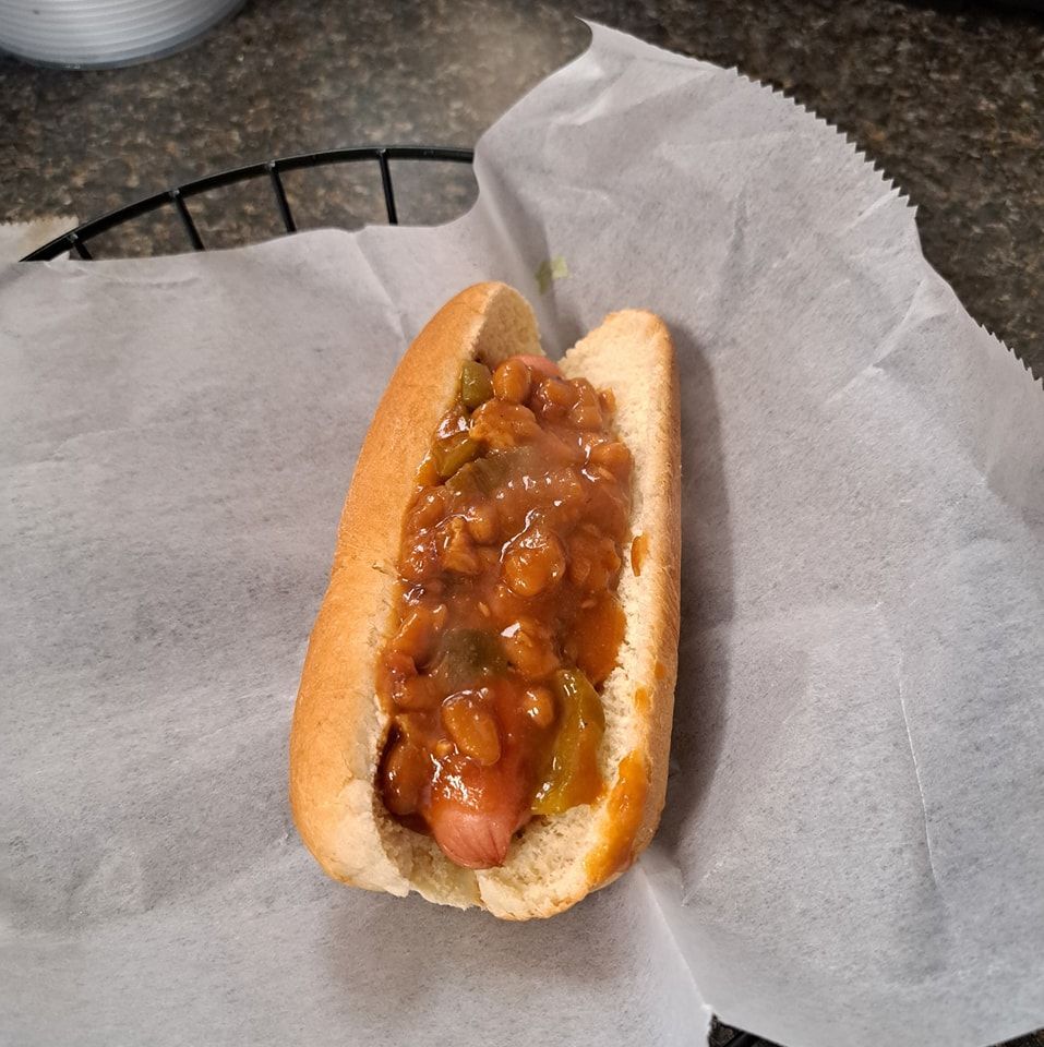 A hot dog with beans and sauce on a bun