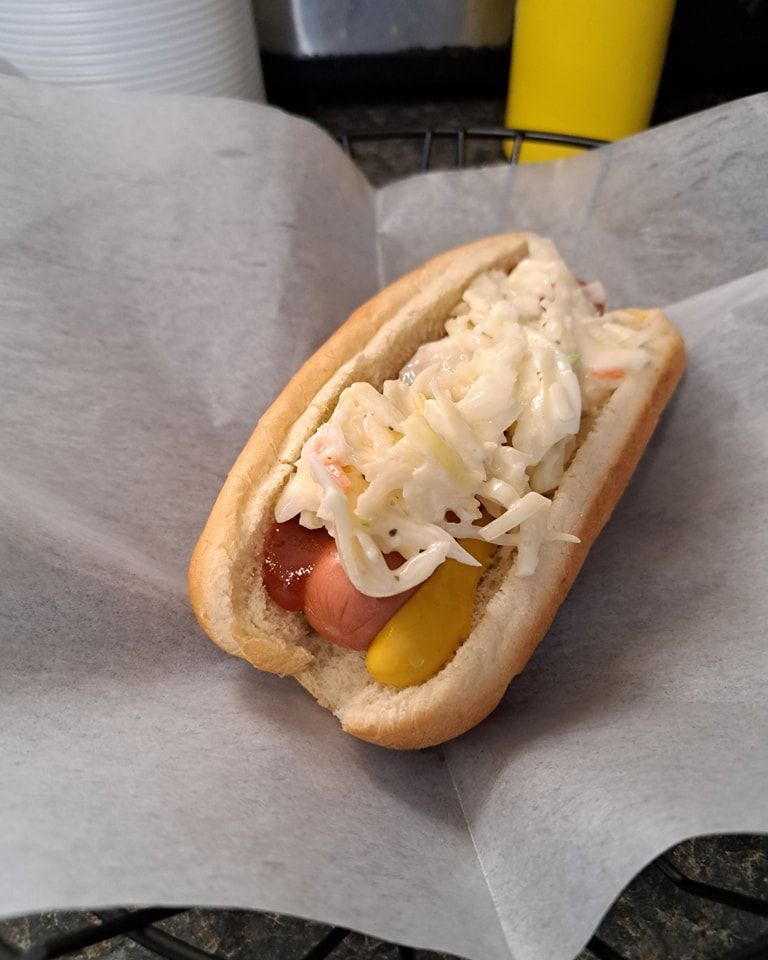 A hot dog with coleslaw and mustard on a bun