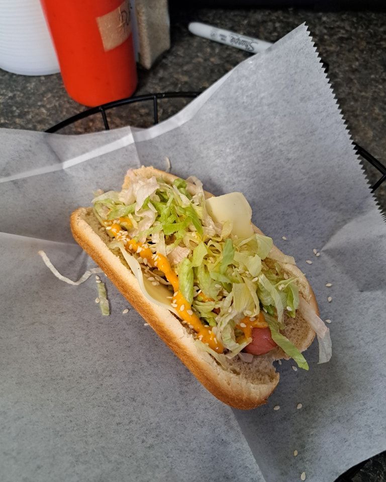 A hot dog with lettuce cheese and sesame seeds on a bun