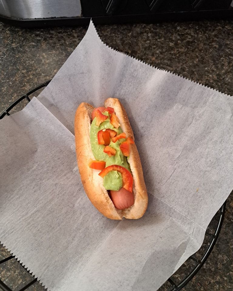 A hot dog with guacamole and tomatoes on it