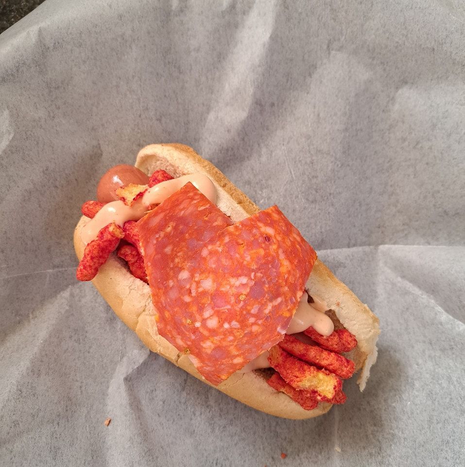 A hot dog with cheese pepperoni and cheetos on it