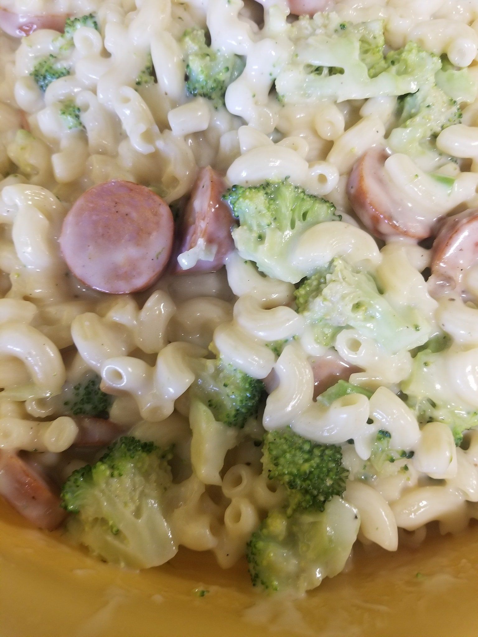 A close up of macaroni and cheese with broccoli and sausage on a plate.