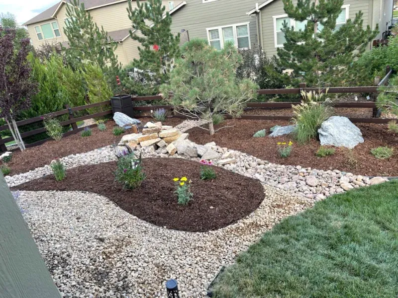 A garden with a wooden fence and rocks in front of a house.